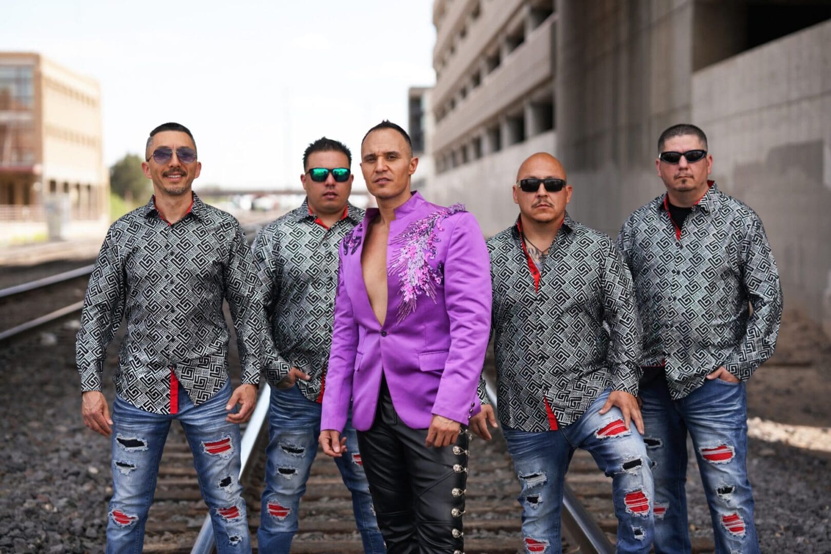 A group of men in purple jackets standing on railroad tracks.